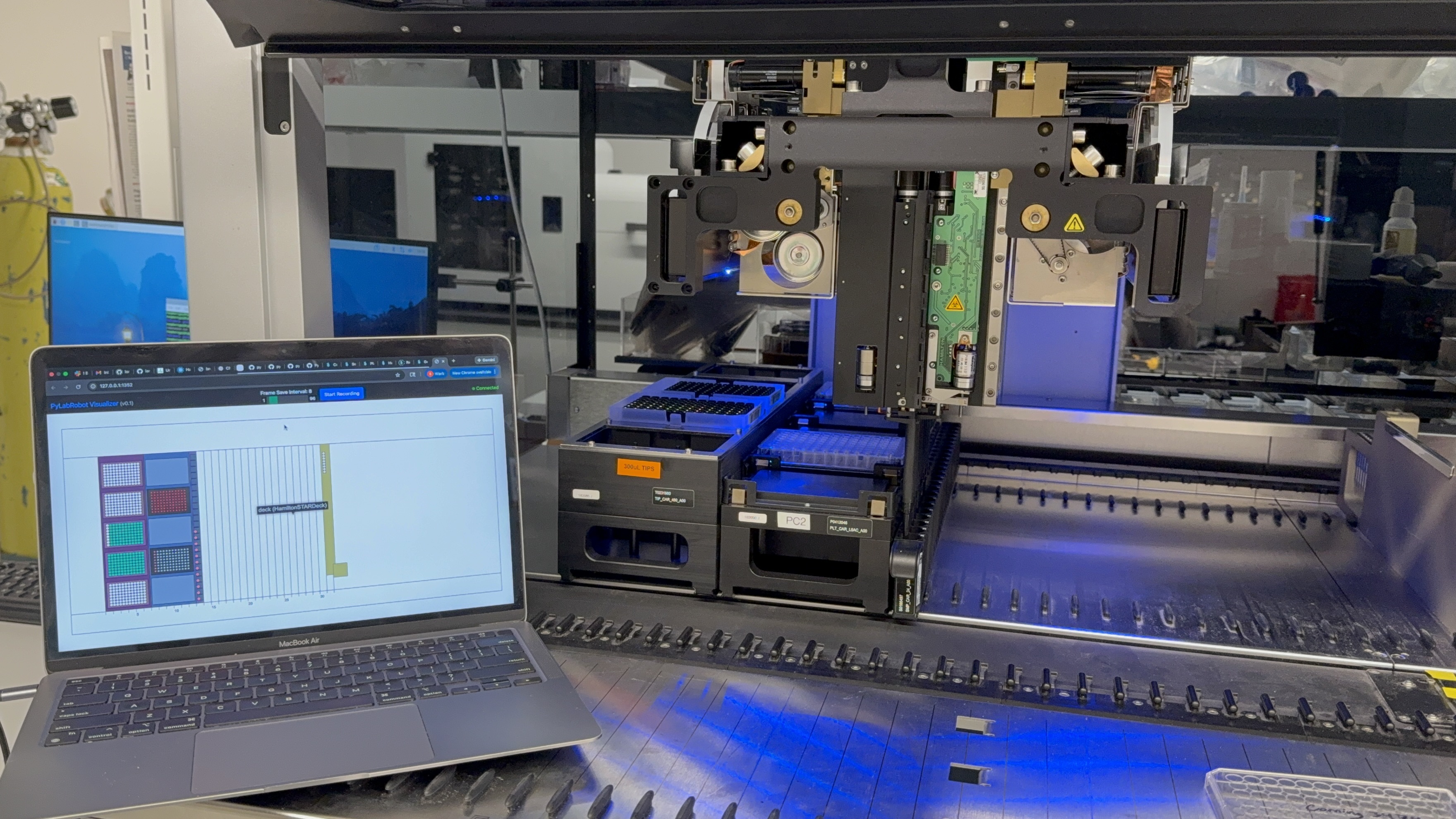 A laptop displaying the PyLabRobot Visualizer beside the physical Hamilton STAR, showing the modeled deck alongside the robot's labware.